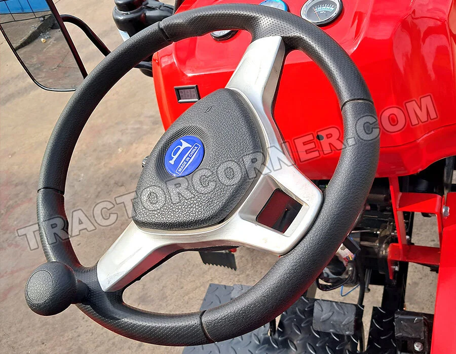 Close-up of a black steering wheel inside a red tractor cockpit, with a blue circular logo at the center.
